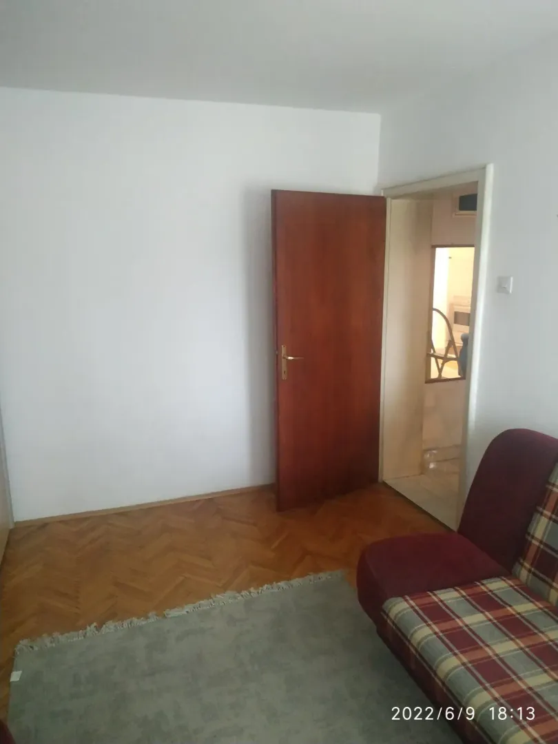 Jednostavna soba sa parketom i kaučem pored otvorenih vrata.