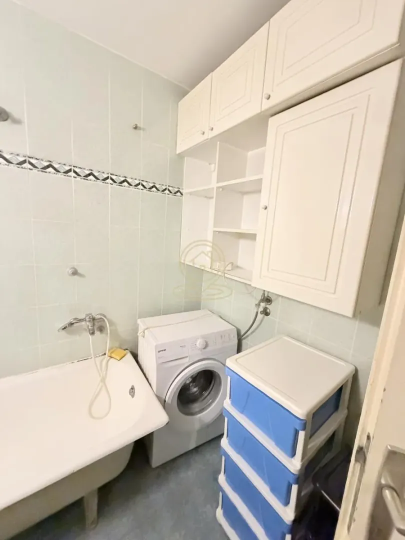Kupatilo opremljeno kadom, veš mašinom i belim zidnim elementima.