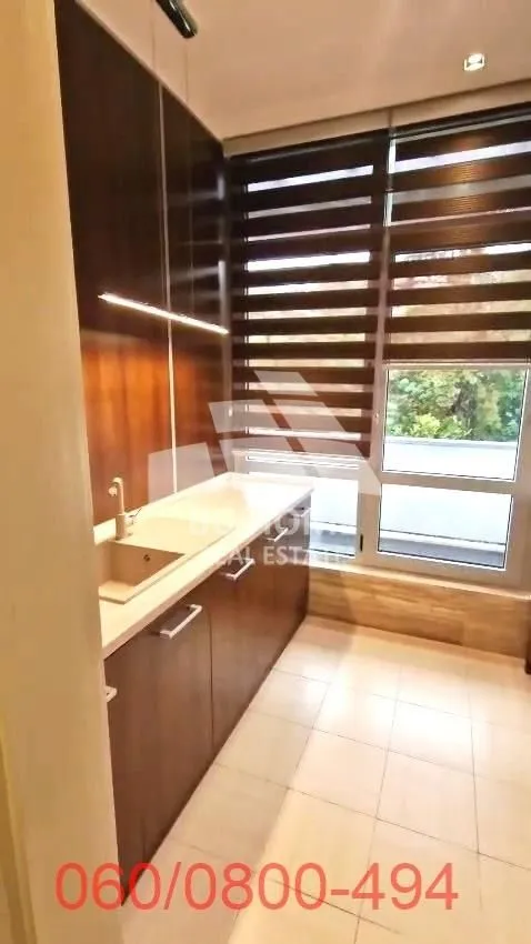 Manja kuhinja sa sudoperom, radnim elementima i prozorom sa roletnama.