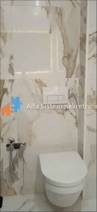 Pogled na moderno opremljeno kupatilo sa konzolnom šoljom i mermernim pločicama.