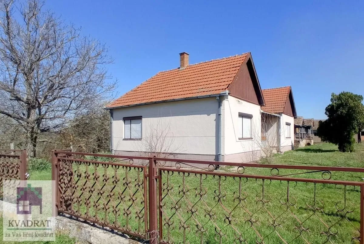 Pogled na spoljašnjost kuće sa dvorištem i ogradom.