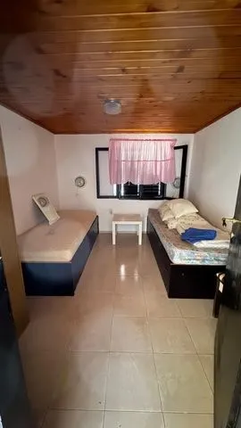 Manja spavaća soba sa dva kreveta i drvenim plafonom.