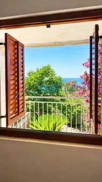 View of the sea and greenery through an open window with wooden shutters. - image 7