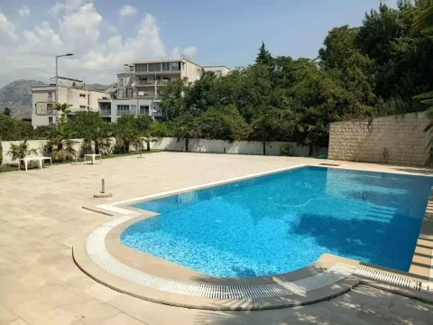 Veliki vanjski bazen sa popločanim platoom za sunčanje i zgradom u pozadini. - image 2