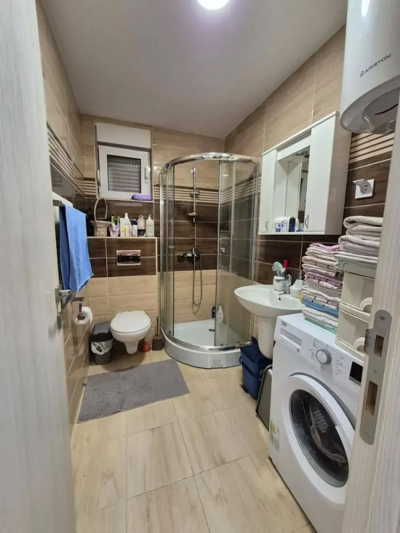 Small bathroom with a shower cabin, washbasin, washing machine, and toilet.