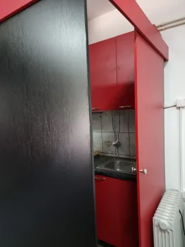 A small kitchen with red cabinets and a single sink. - image 10