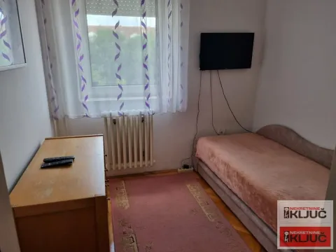Manja spavaća soba sa krevetom, komodom i televizorom na zidu. - image 4