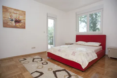 Svijetla spavaća soba sa crvenim krevetom, parketom i izlazom na balkon. - image 10