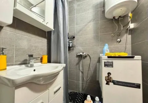 Manje kupatilo sa umivaonikom, tuš kabinom i veš mašinom obloženo sivim pločicama. - image 9