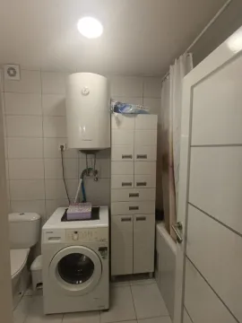 A functional bathroom with a washing machine, water heater, and a tall storage cabinet. - image 7