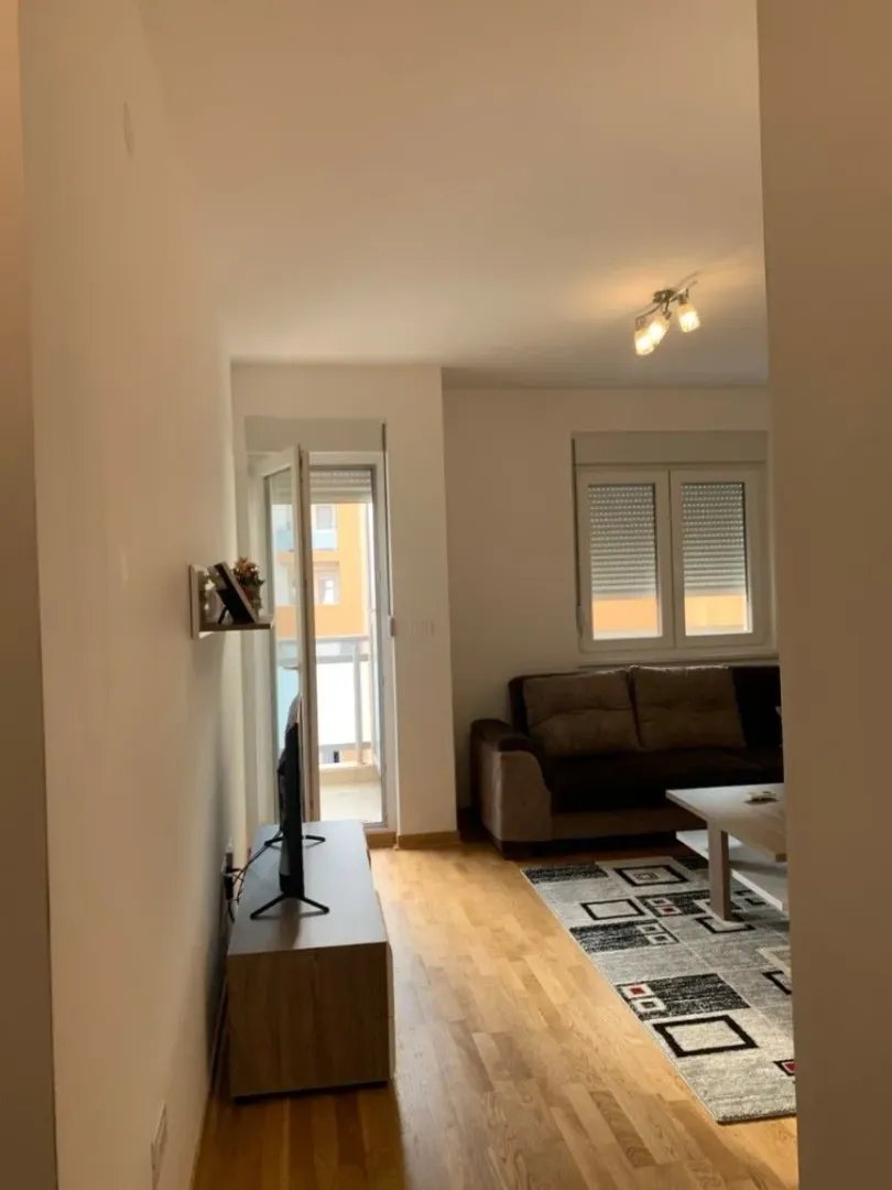 Bright living room with a brown sofa, wooden floors, and access to a balcony.