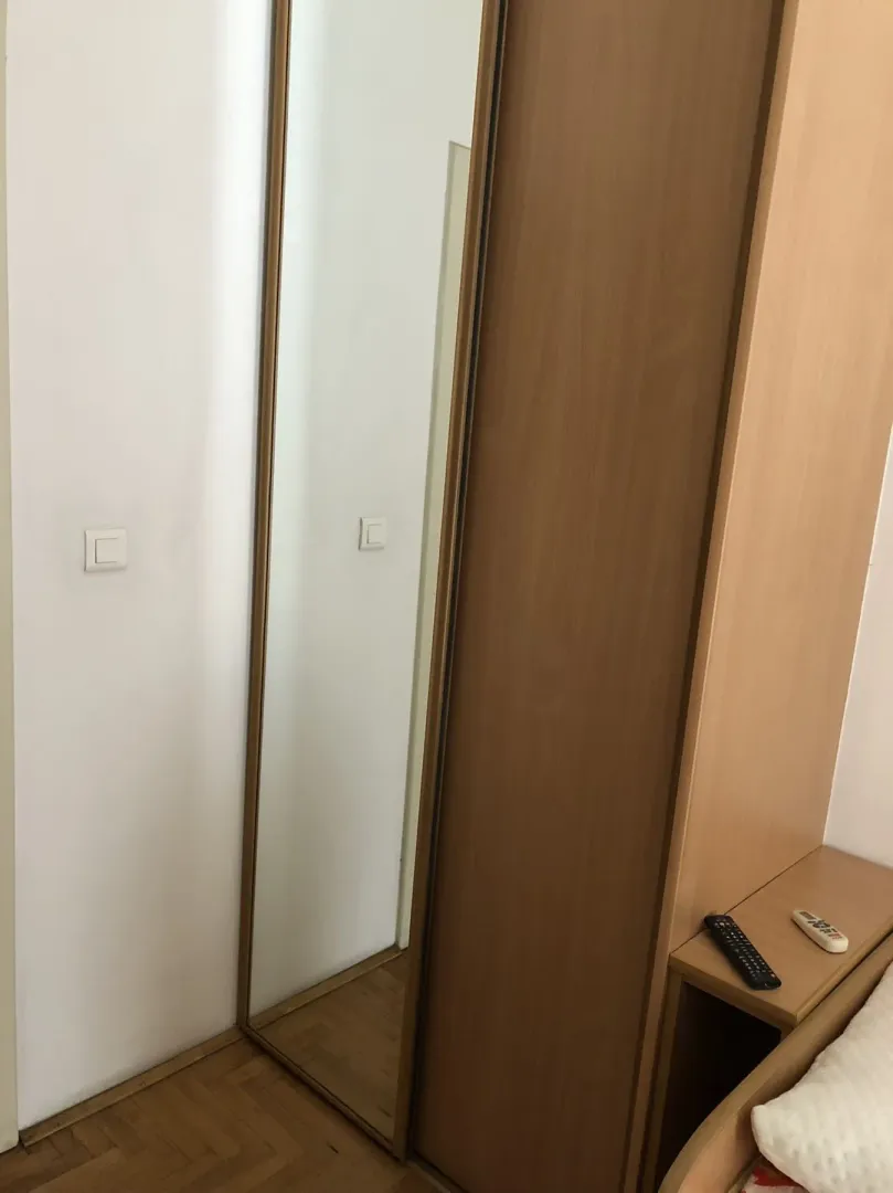 Wooden wardrobe with a built-in mirror next to a bed.
