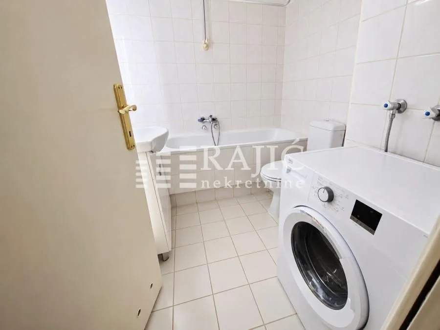 Smaller bathroom with a bathtub, washbasin, and washing machine.