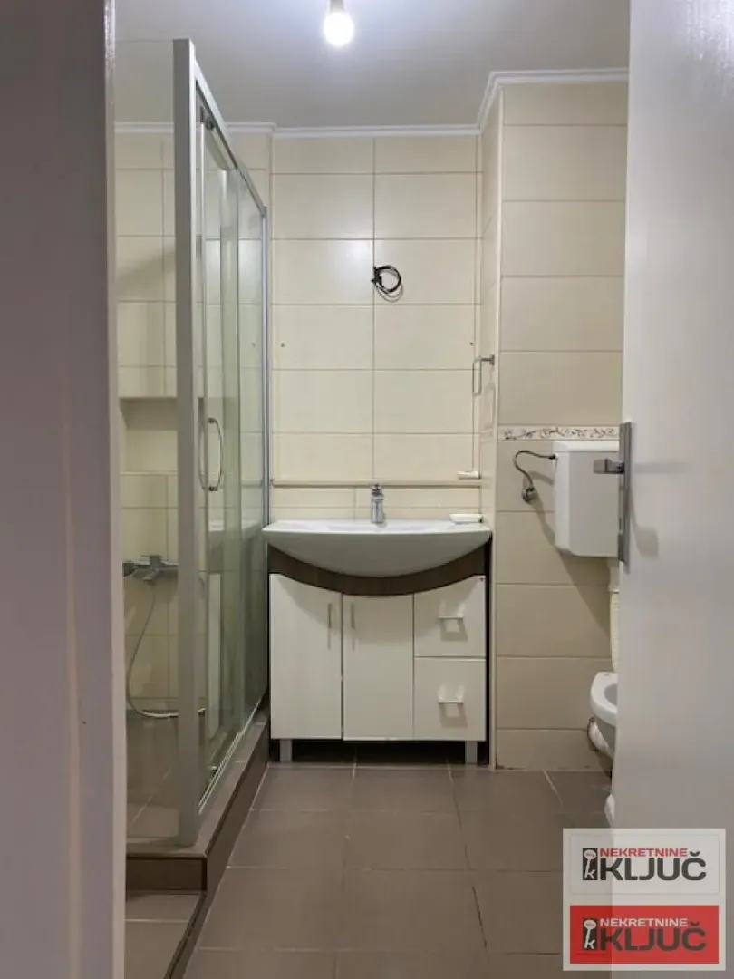 Pogled na kupatilo sa tuš kabinom, umivaonikom i WC šoljom.