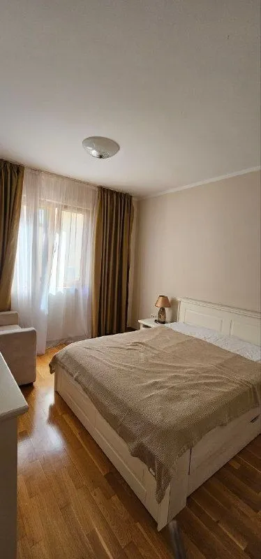 Spavaća soba sa bračnim krevetom, noćnim stočićem i prozorom sa zavjesama.