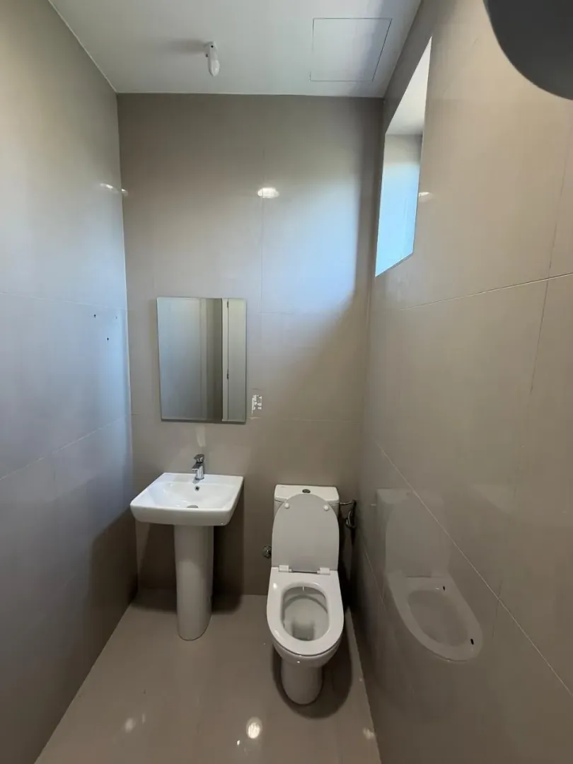 Smaller bathroom with a sink, mirror, and toilet tiled with ceramic tiles.