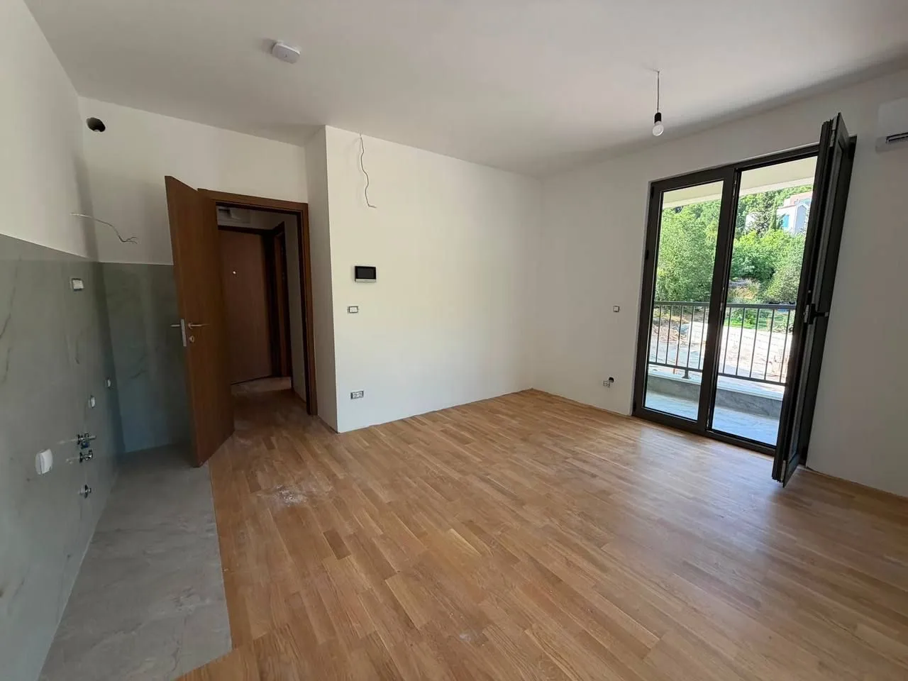Prazna soba sa parketom i izlazom na balkon.