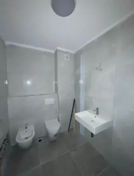 Pogled na moderno opremljeno kupatilo sa sijelim pločicama, umivaonikom i sanitarijama. - image 11