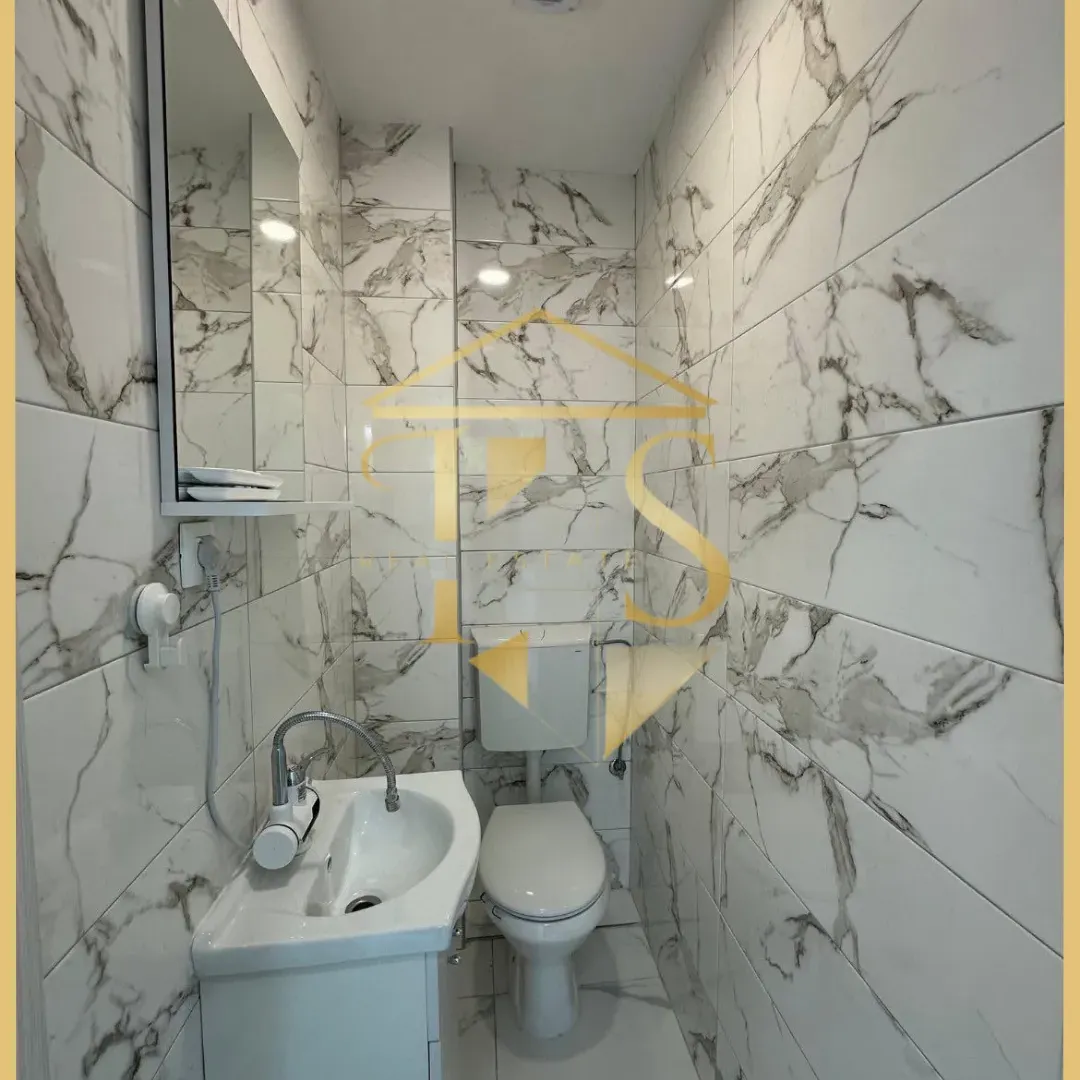 Small bathroom lined with marble tiles featuring a sink and a toilet.