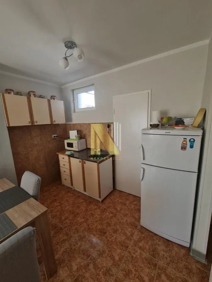Manja kuhinja sa elementima, frižiderom i trpezarijskim stolom.