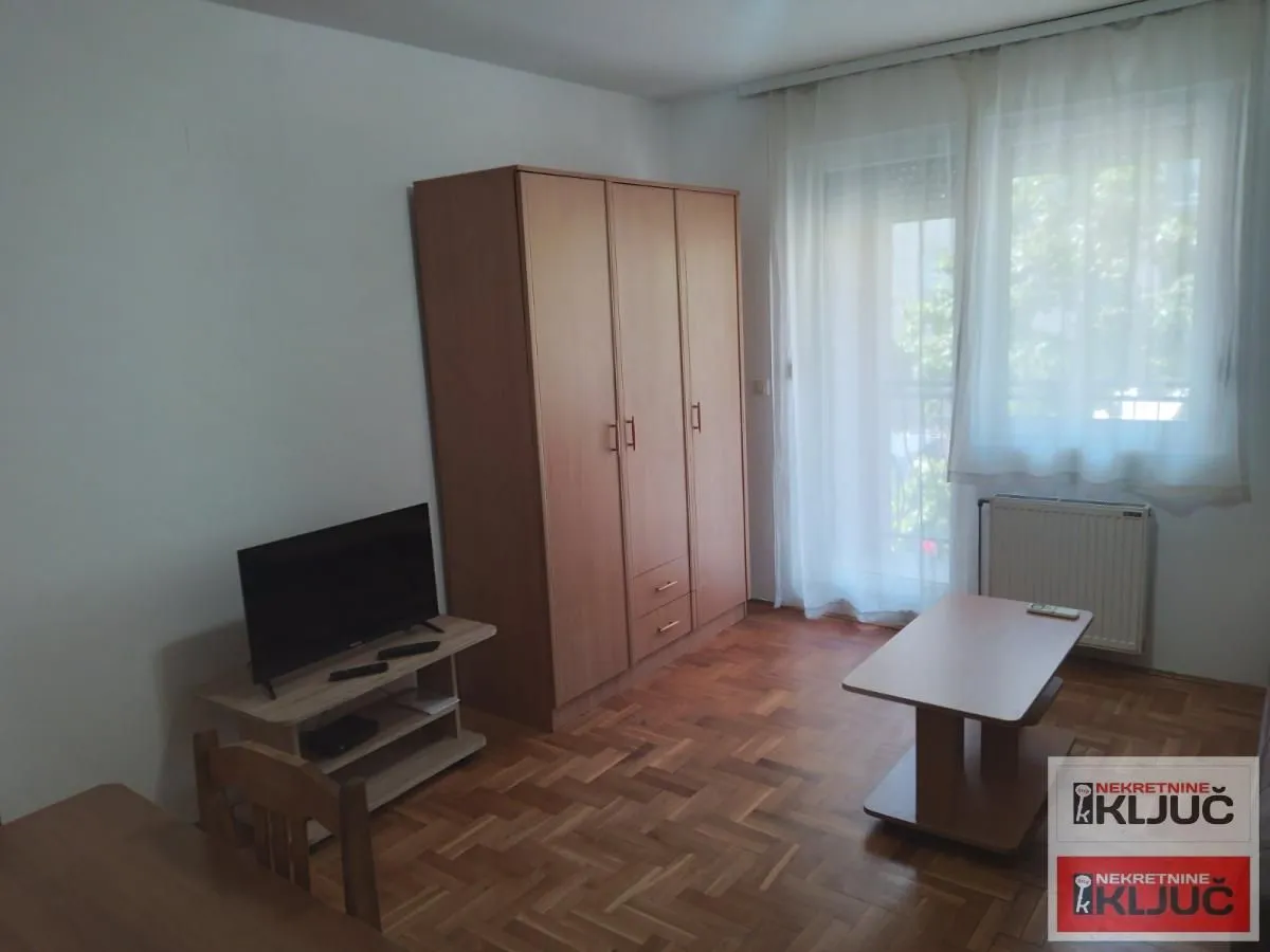 Dnevna soba sa ormanom, televizorom i izlazom na terasu.