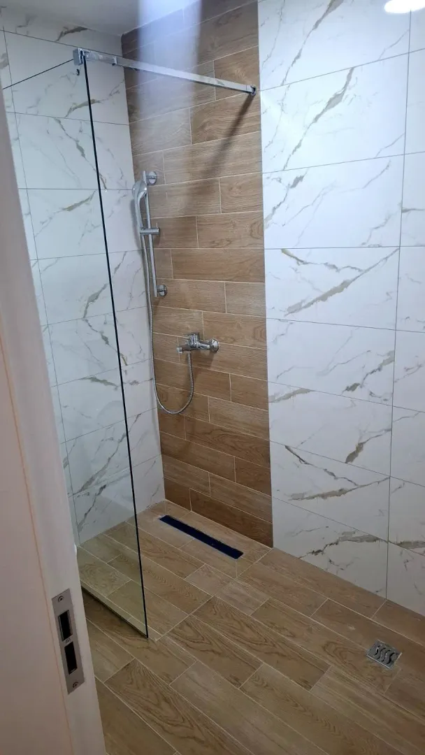 Moderne tuš kabina sa staklenom pregradom i kombinacijom pločica.