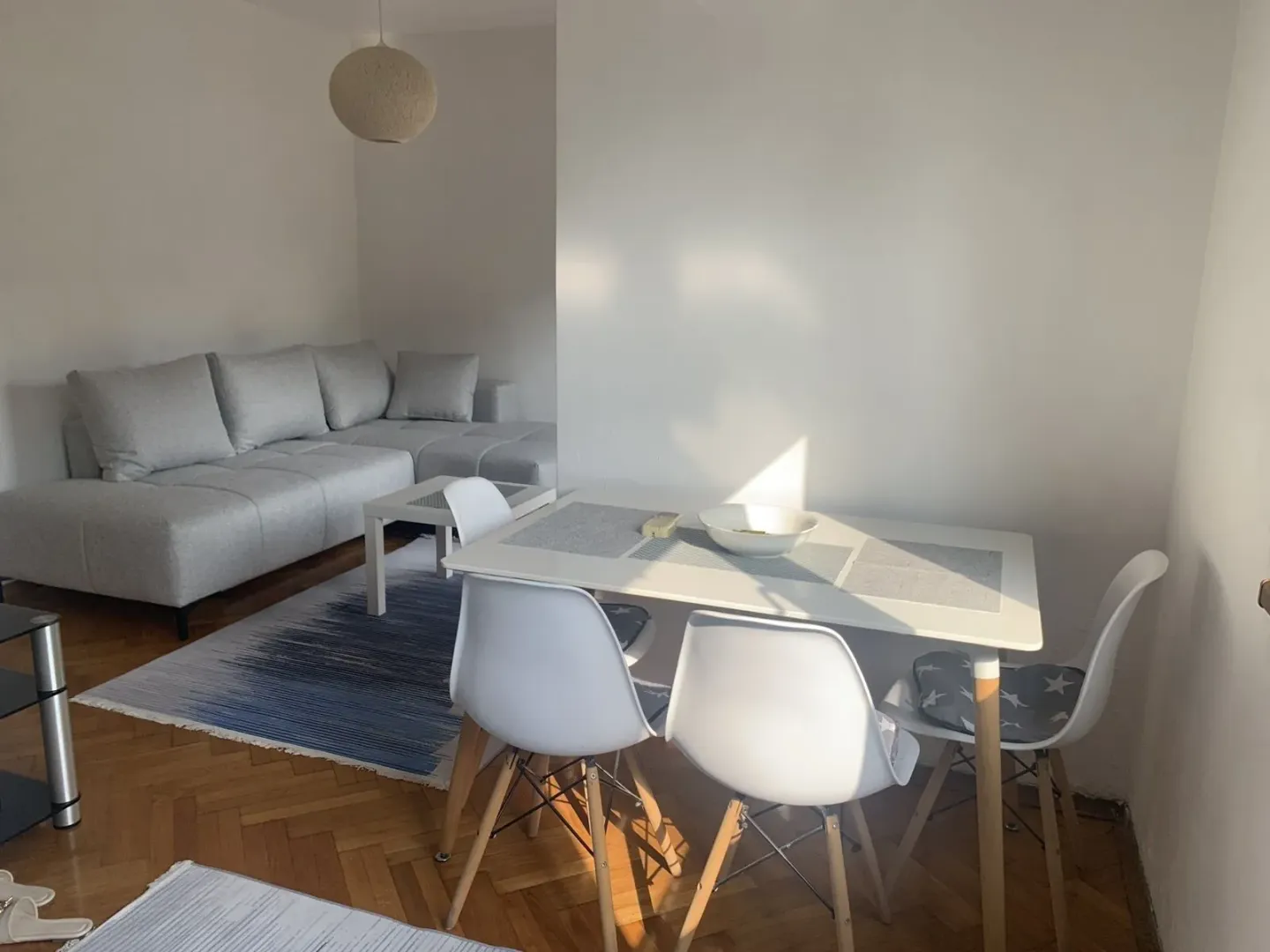 Svijetla dnevna soba sa trpezarijskim stolom i sivom ugaonom garniturom.