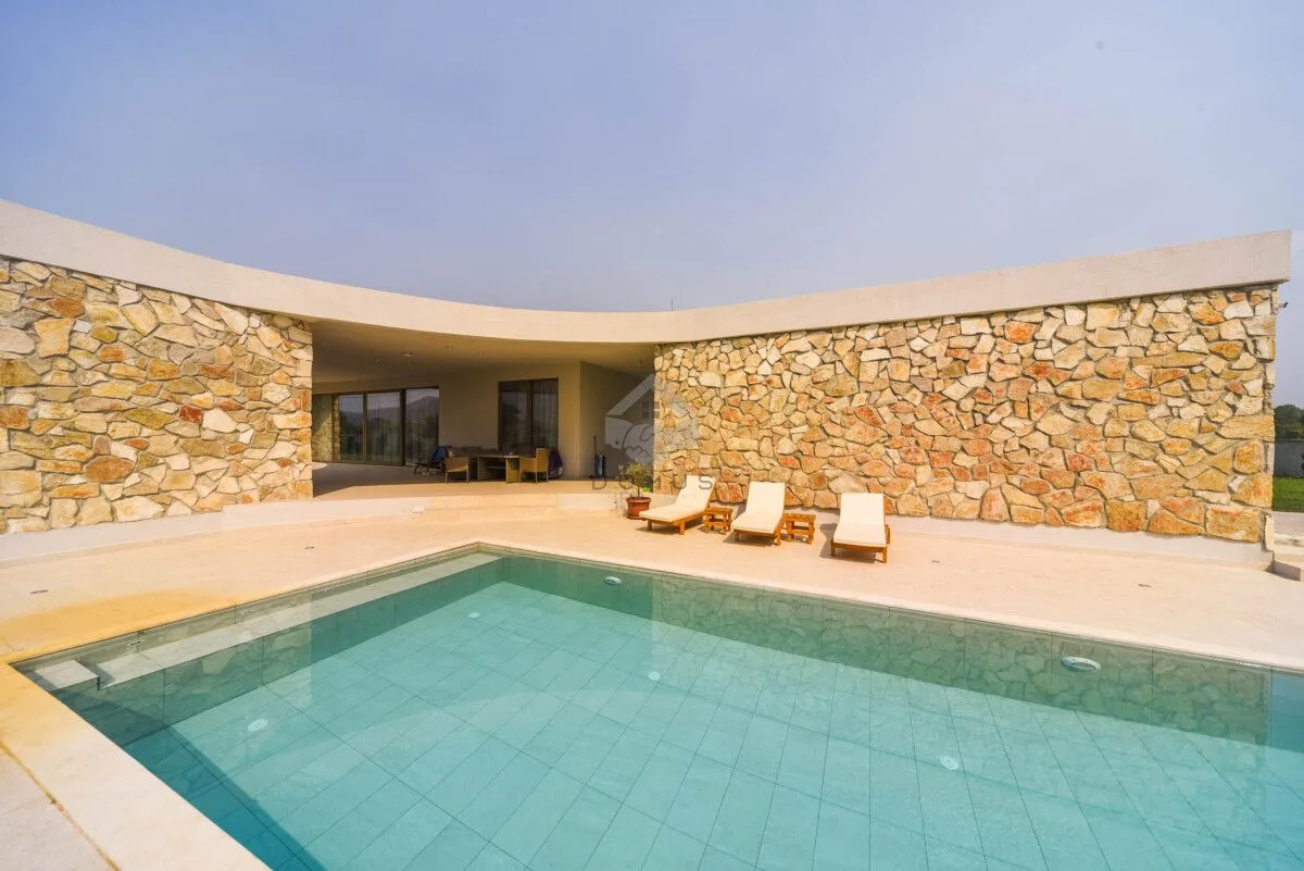 Swimming pool with a sun terrace and sun loungers in front of a modern house with a stone facade.