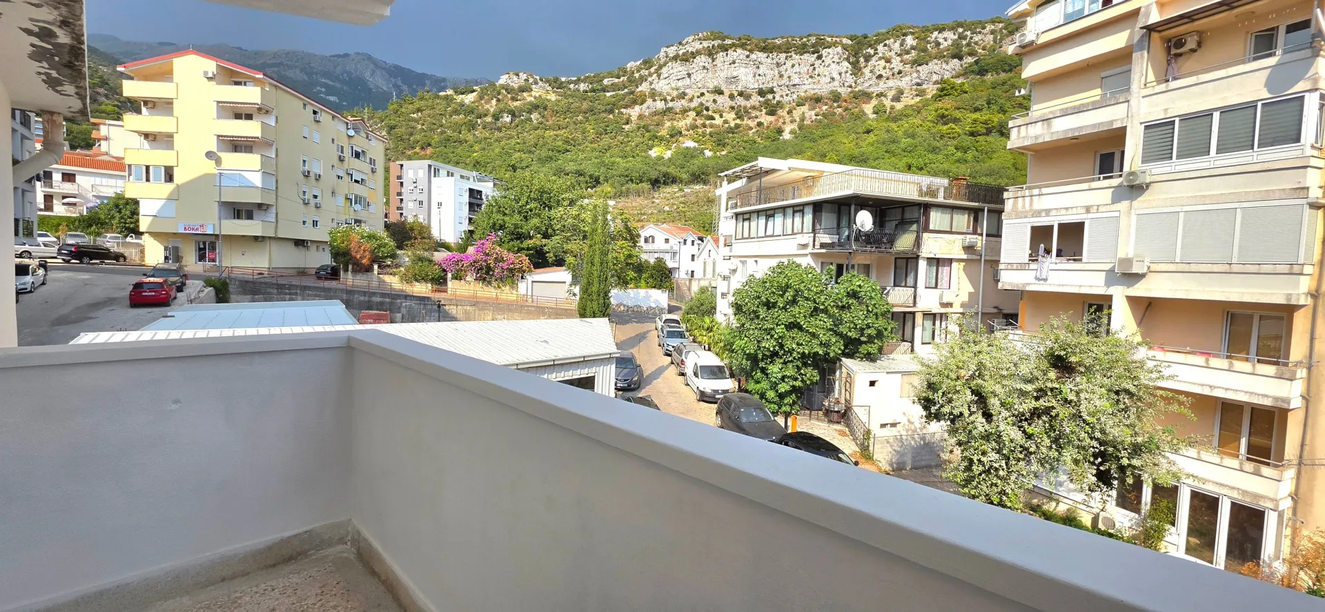 Pogled sa balkona na okolne zgrade, ulicu i brdo u pozadini.
