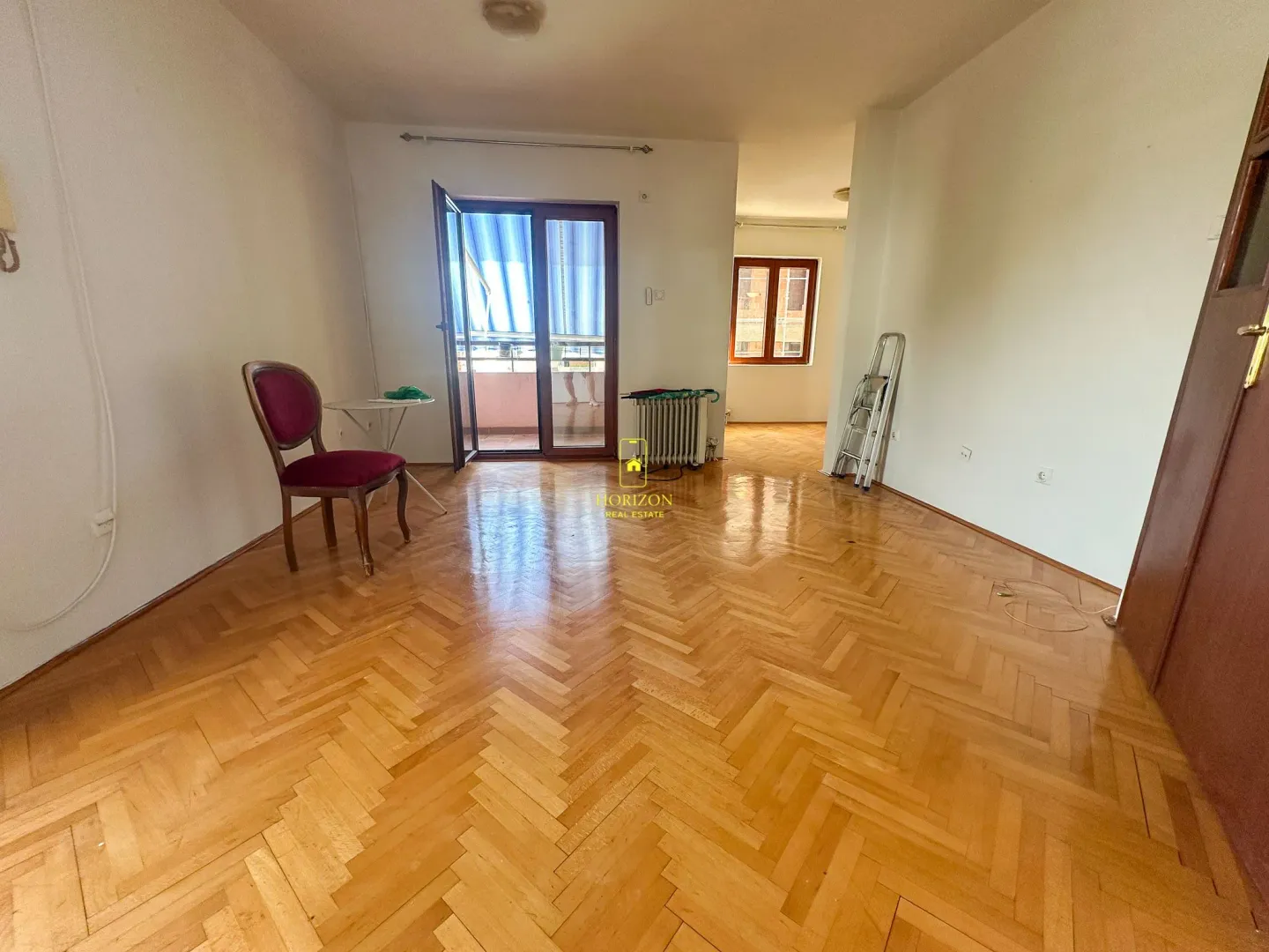 Prazna prostorija sa drvenim parketom i izlazom na terasu.