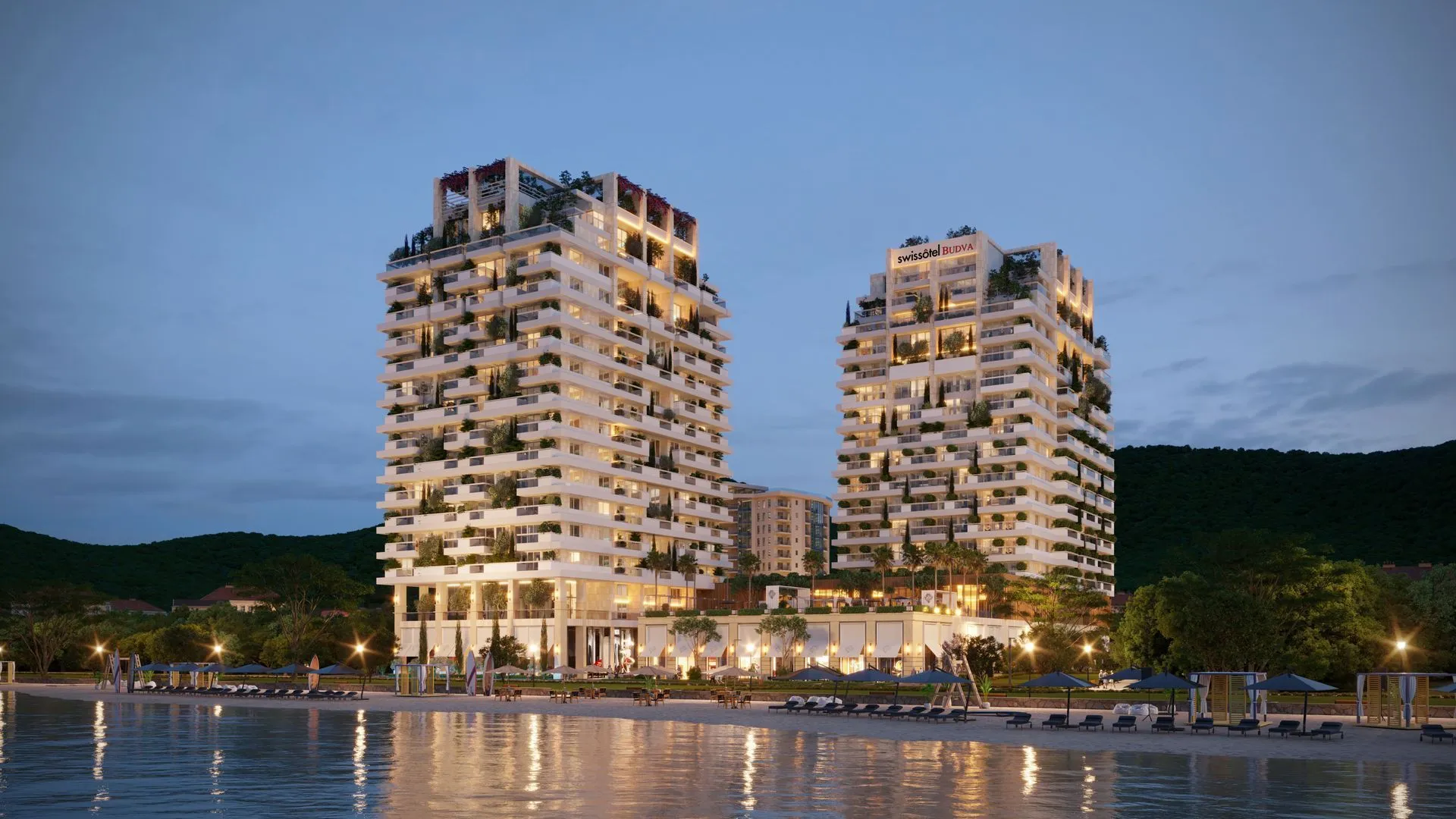 Pogled sa plaže na osvijetljene moderne stambene zgrade u večernjim satima.