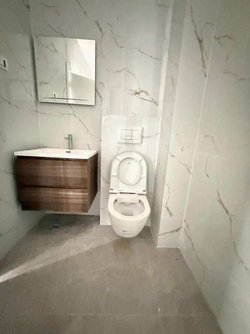 Modern bathroom with a sink, mirror, and toilet lined with marble tiles.