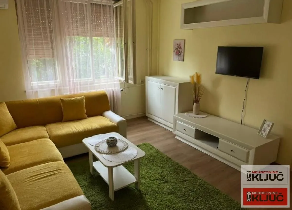 Dnevna soba sa garniturom, stočićem i televizorom na zidu.