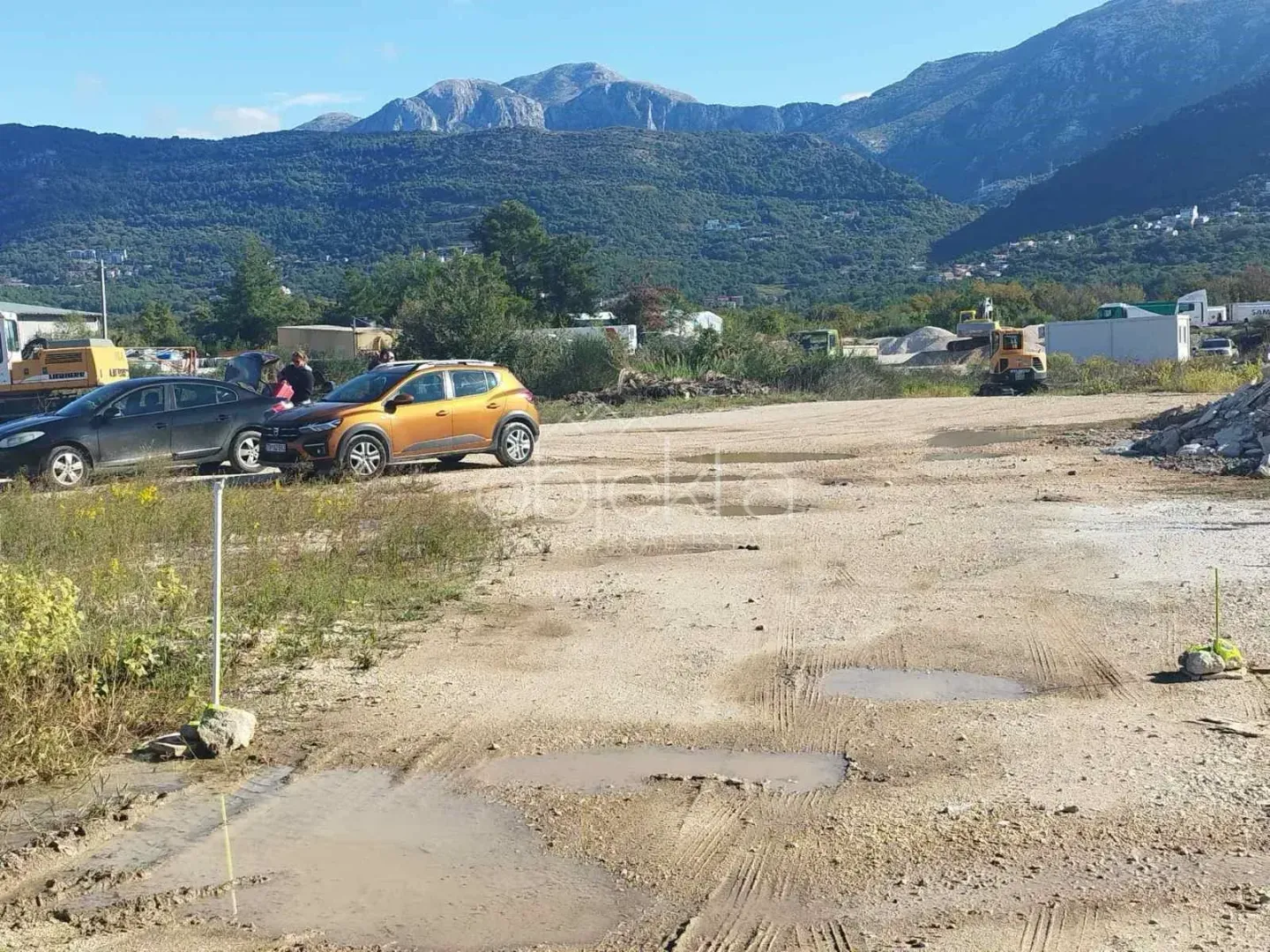 Pogled na plac i okolne planine sa parkiranim automobilima.