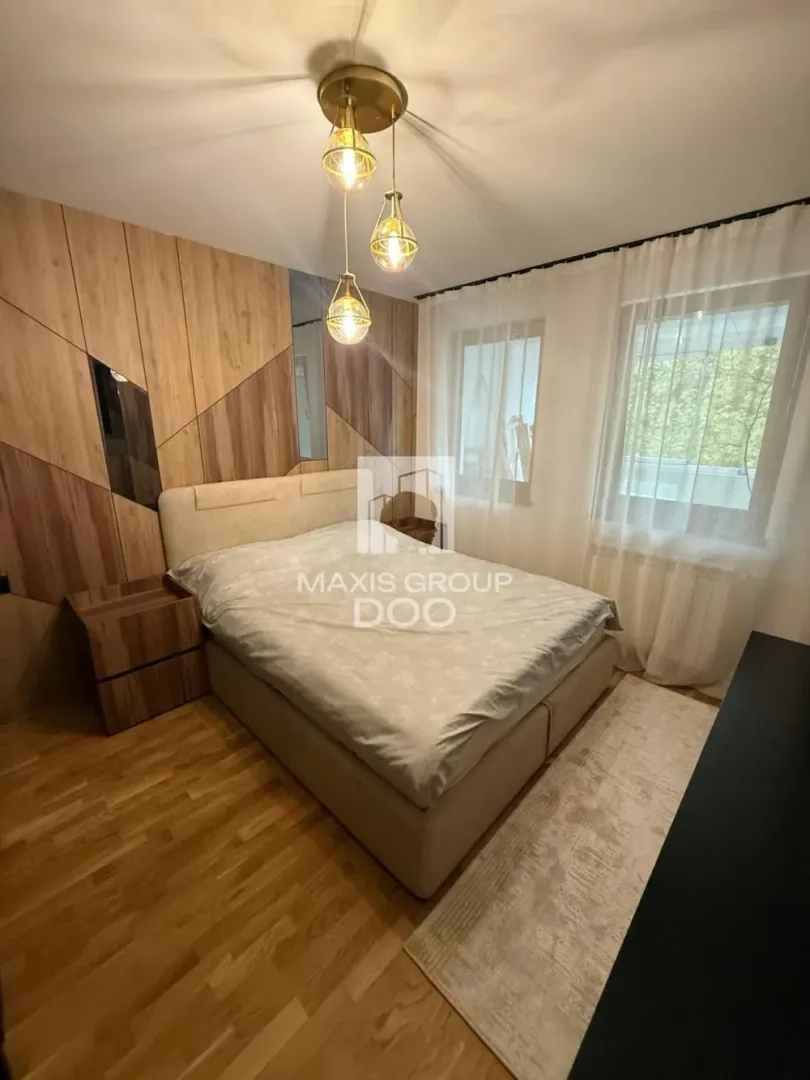 Nameštena spavaća soba sa bračnim krevetom, drvenim zidnim panelima i lusterom.