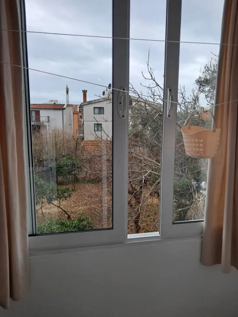 Pogled kroz prozor na okolne zgrade i drveće.