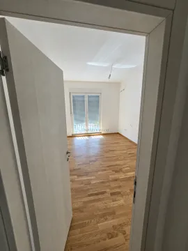 Prazna soba sa drvenim parketom i balkonskim vratima, gledano kroz otvorena vrata. - image 13
