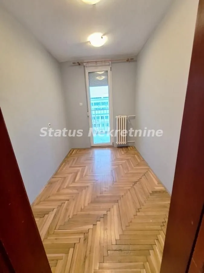 Prazna soba sa drvenim parketom i izlazom na balkon.