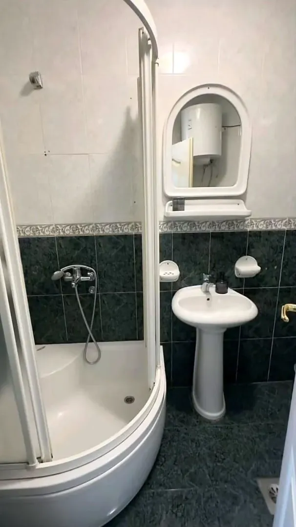 Manje kupatilo sa tuš kabinom, umivaonikom i ogledalom.