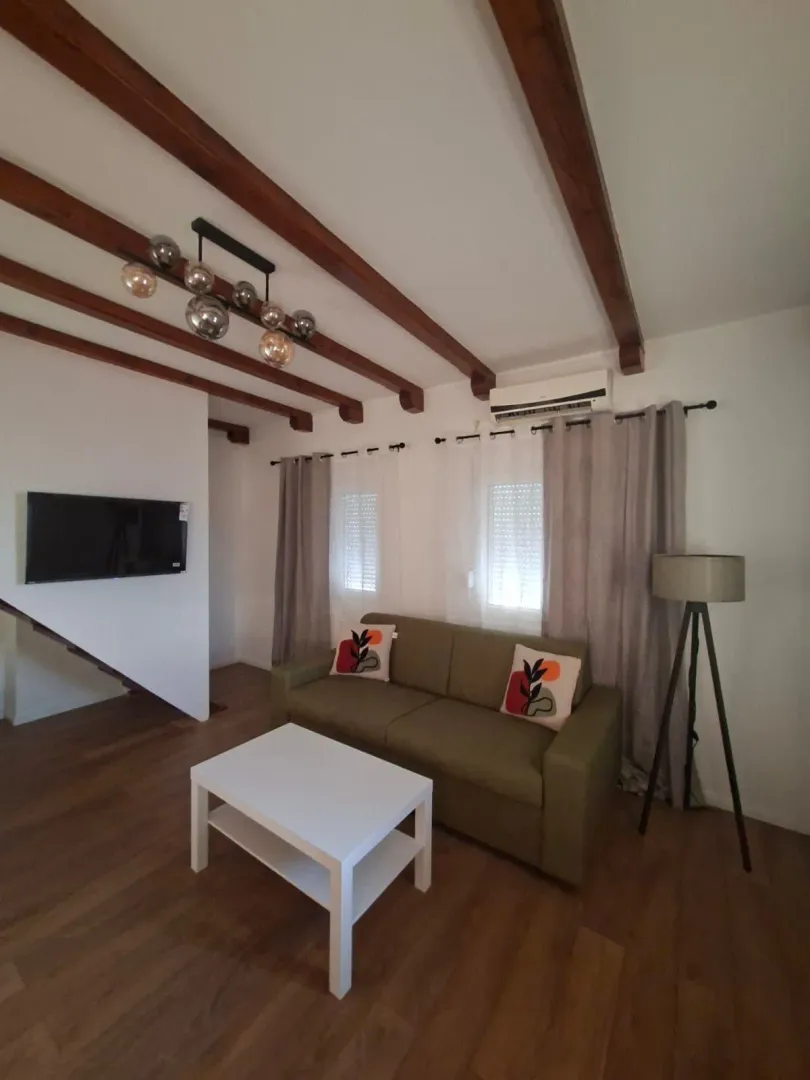 Living room with a sofa, wooden ceiling beams, and a modern chandelier.