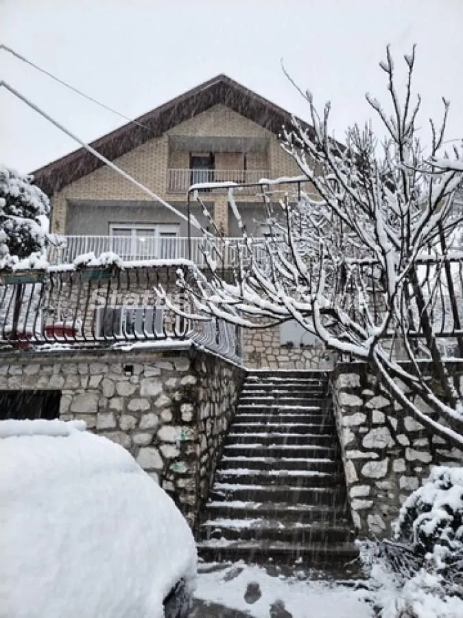 Exterior view of the house with stairs and yard during snowfall.