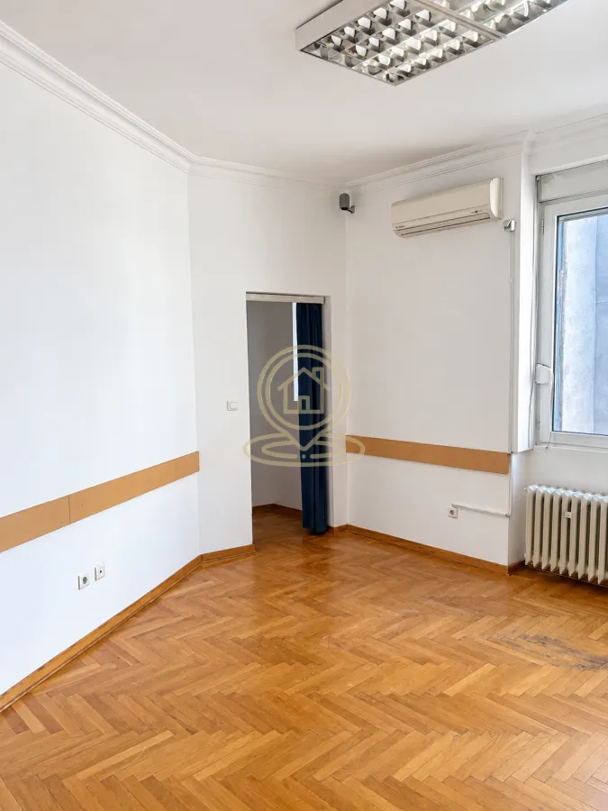 Empty office room with white walls, parquet flooring, and an air conditioning unit.