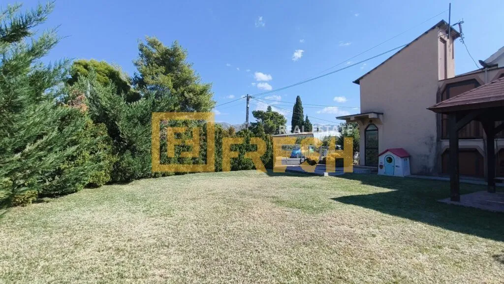 Prostrano travnato dvorište sa zelenilom i kućom u pozadini.