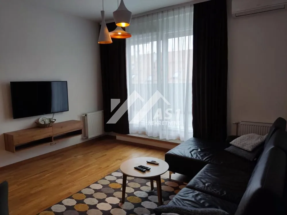Dnevna soba sa garniturom za sedenje, TV-om i velikim prozorom.