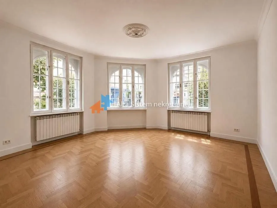 Empty room with hardwood flooring and large windows.
