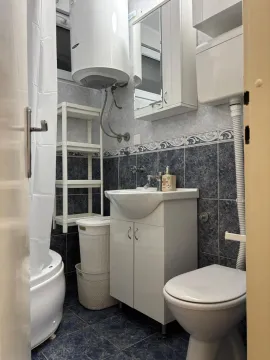 Smaller bathroom with a washbasin, toilet, shower cabin, and water heater. - image 12