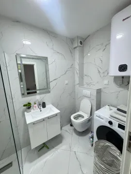 Savremeno opremljeno kupatilo sa bijelim mermernim pločicama, umivaonikom, WC šoljom i mašinom za veš. - image 7