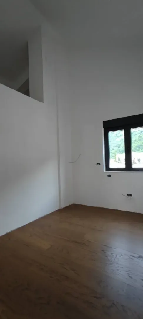 Prazna, novoizgrađena soba sa drvenim podom i bijelim zidovima.
