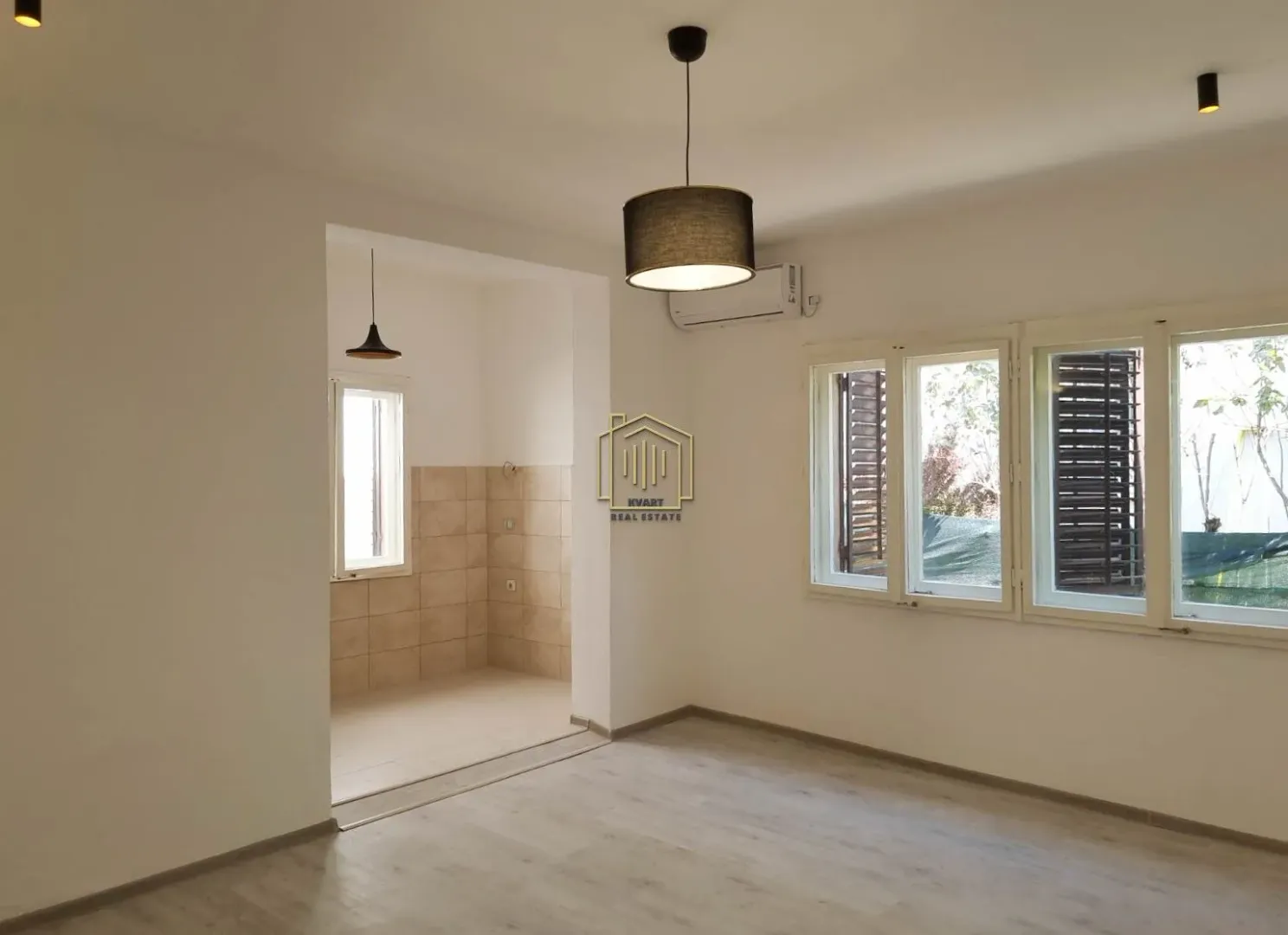 Empty living room with a view of part of the kitchen and windows with shutters.