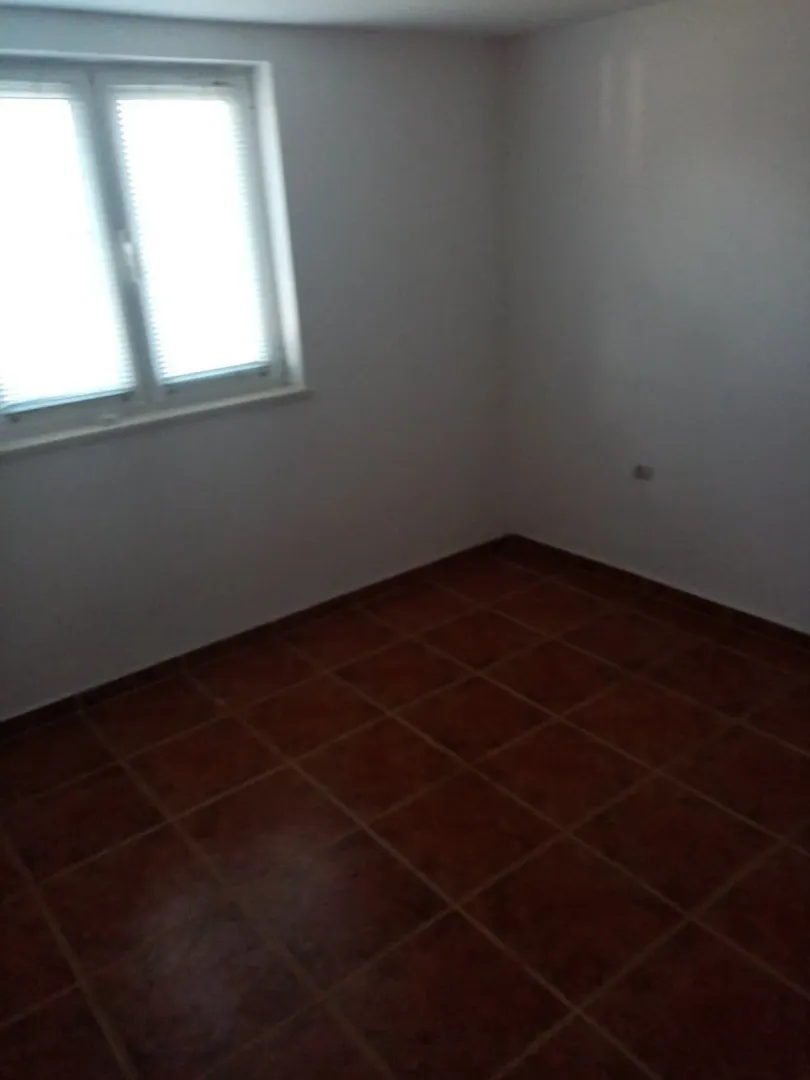 An empty room with dark tiled flooring and a single window.